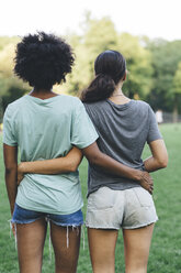 Rückenansicht von zwei Frauen, die Arm in Arm in einem Park stehen - GIOF01979