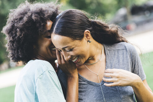 Two young women whispering in a park - GIOF01981