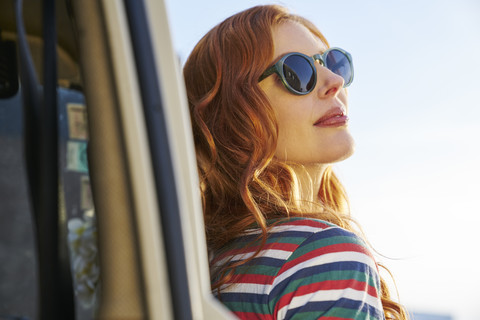 Junge Frau mit Sonnenbrille lehnt an einem Auto, lizenzfreies Stockfoto