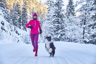 Österreich, Tirol, Karwendel, Rißtal, Frau joggt mit Hund im Winterwald - MRF01697