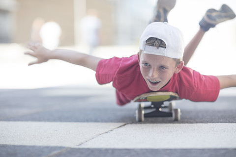 Junge fährt Skateboard auf der Straße, auf dem Bauch liegend, lizenzfreies Stockfoto