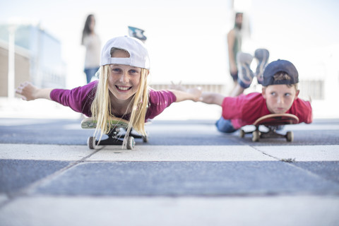 Kinder, die auf der Straße Skateboard fahren und auf dem Bauch liegen, lizenzfreies Stockfoto