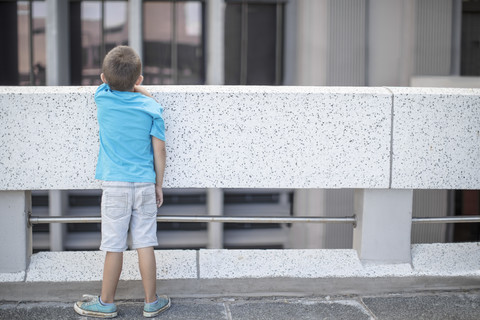 Junge steht auf einer Brücke und schaut über das Geländer, Rückansicht, lizenzfreies Stockfoto