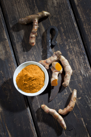 Ganze und geschnittene Kurkuma, Schale mit Kurkuma und ein altes Messer auf dunklem Holz, lizenzfreies Stockfoto