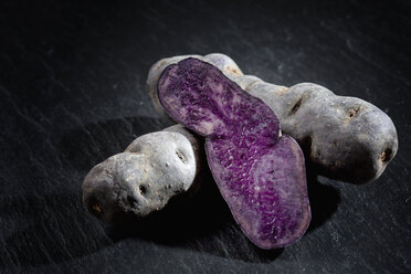 Ganze und in Scheiben geschnittene violette Kartoffeln auf Schiefer - CSF27894