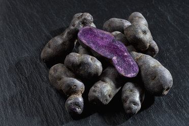 Ganze und in Scheiben geschnittene violette Kartoffeln auf Schiefer - CSF27896