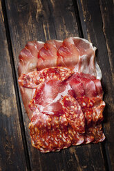 Slices of Spanish salami and Italian ham on dark wood - CSF27912
