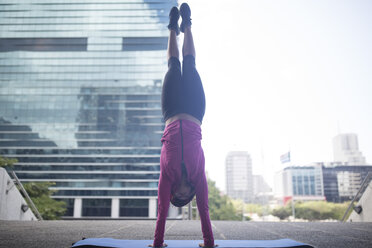 Young woman doing a handstand on gymnastics mat in the city - ZEF12932