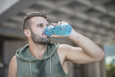 Sportler macht eine Pause in der Stadt und trinkt Wasser aus einer Flasche, lizenzfreies Stockfoto