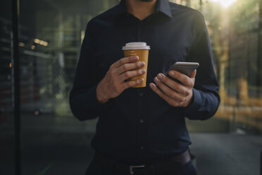 Businessman holding takeaway coffee and smartphone - KNSF01049