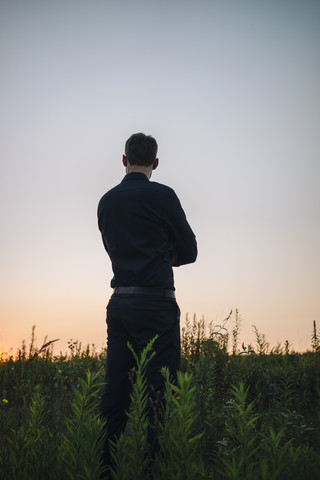 Geschäftsmann steht in einem ländlichen Feld bei Sonnenuntergang, lizenzfreies Stockfoto