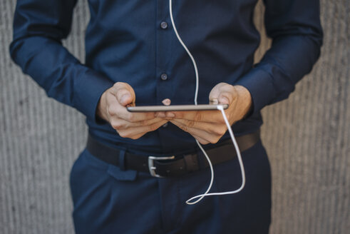 Businessman holding tablet with connected earphones - KNSF01057