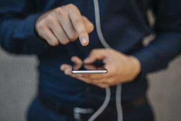 Businessman using smartphone with connected earphones - KNSF01063