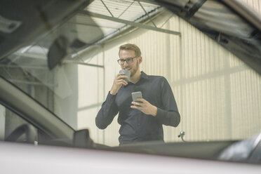 Lächelnder Geschäftsmann mit Mobiltelefon und Tasse Kaffee - KNSF01066