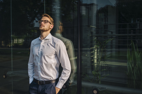 Geschäftsmann lehnt an einer Glaswand, lizenzfreies Stockfoto