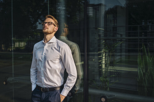 Businessman leaning against glass wall - KNSF01074