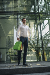 Businessman holding paper bags in front of building - KNSF01079