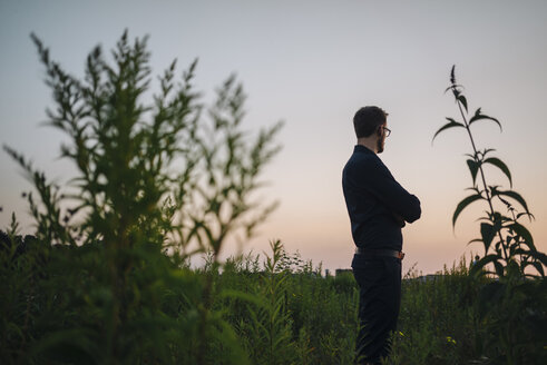 Businessman standing in rural field at sunset - KNSF01087