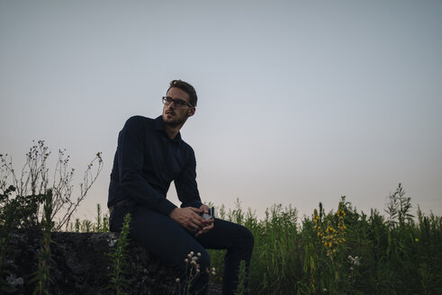 Businessman sitting in rural field at dusk - KNSF01090