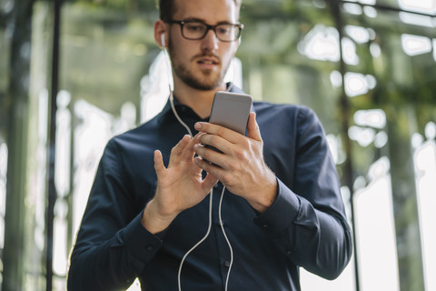 Geschäftsmann hält Smartphone mit angeschlossenen Kopfhörern, lizenzfreies Stockfoto