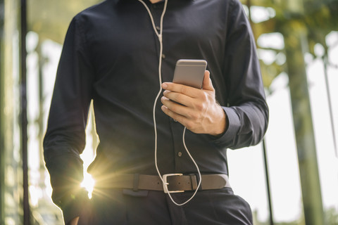 Businessman holding smartphone with connected earphones stock photo