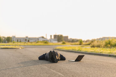 Businessman lying on a road next to laptop - KNSF01125