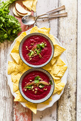 Two bowls of beetroot soup garnished with apple slices, peanuts and flat leaf parsley served with tortilla chips - SARF03206