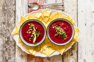 Two bowls of beetroot soup garnished with apple slices, peanuts and flat leaf parsley served with tortilla chips - SARF03207