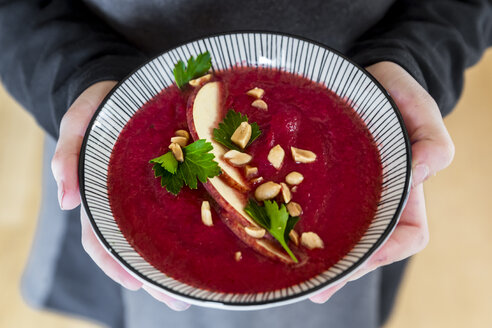 Mädchenhände halten eine Schüssel Rote-Bete-Suppe, garniert mit Apfelscheiben, Erdnüssen und glatter Petersilie - SARF03209