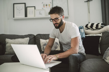 Young man sitting on couch, using laptop on coffee table - RAEF01740