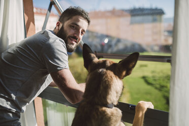 Junger Mann steht mit seinem Hund am Fenster und wartet - RAEF01749
