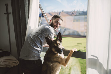 Young man standing at window with his dog, waiting - RAEF01750