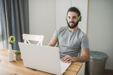 Junger Mann mit Kopfhörern, der einen Laptop benutzt - RAEF01755