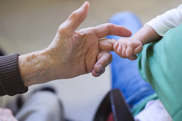 Baby hält den Finger der Hand seiner Urgroßmutter - DIGF01523