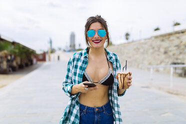 Junge Frau am Strand mit einer Tasse Kaffee und einem Smartphone - GIOF02008