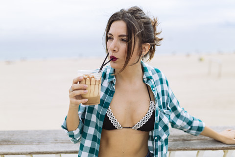 Junge Frau am Strand trinkt eine Tasse Kaffee, lizenzfreies Stockfoto