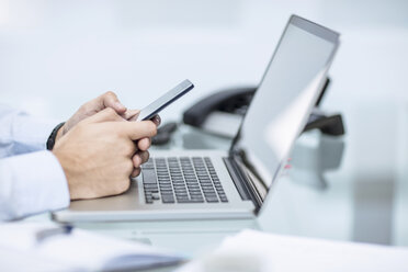 Businessman using smart phone at desk with laptop - ZEF12969