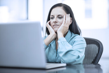 Frau mit dem Kopf in den Händen sitzt in einem Büro hinter Computer - ZEF12977