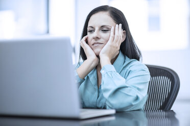 Woman with her head in her hands sitting in a office behind computer - ZEF12977