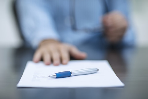 Person sitzt am Schreibtisch mit Dokumenten und einem Stift, lizenzfreies Stockfoto