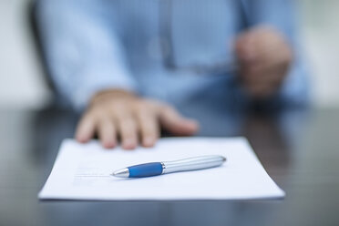 Person sitzt am Schreibtisch mit Dokumenten und einem Stift - ZEF12983