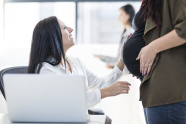 Frau im Büro berührt den Bauch einer schwangeren Kollegin - ZEF12988