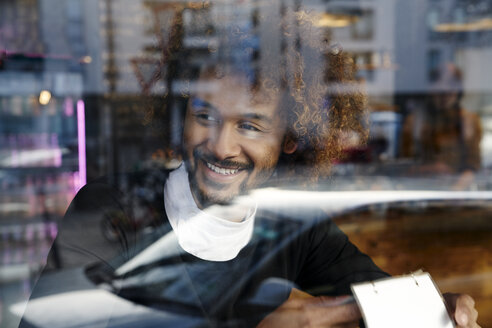 Porträt eines lächelnden jungen Mannes hinter einer Fensterscheibe - FMKF03492