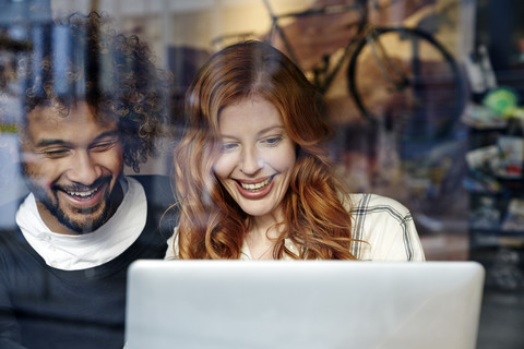 Happy young couple using laptop behind windowpane stock photo