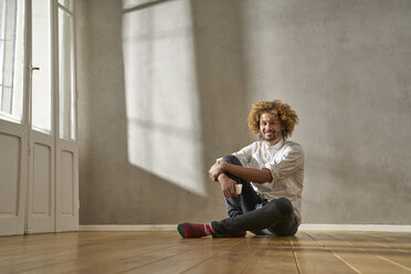 Smiling young man sitting in a room - FMKF03501