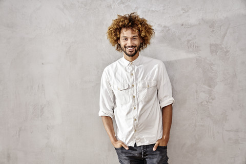 Portrait of smiling young man standing at grey wall stock photo