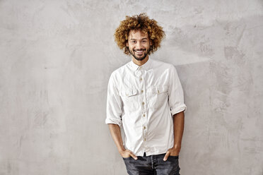 Portrait of smiling young man standing at grey wall - FMKF03503