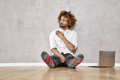 Young man sitting in a room next to laptop stock photo