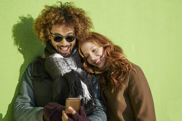 Glückliches junges Paar schaut auf Handy an grüner Wand - FMKF03508
