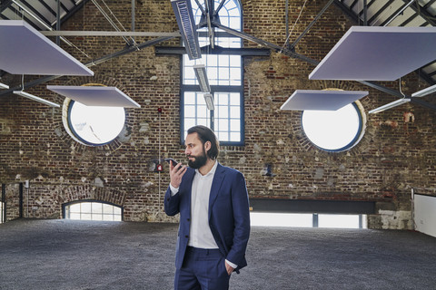 Geschäftsmann benutzt Mobiltelefon in einem Loft, lizenzfreies Stockfoto